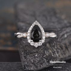 a pear shaped black and white diamond engagement ring on top of a rock with diamonds around it