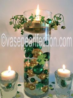 a glass vase filled with lots of green and gold balls next to two lit candles