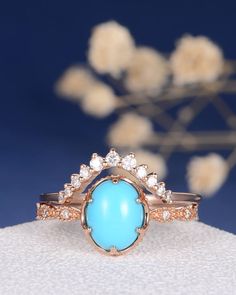 a turquoise stone and diamond ring sitting on top of a white cloth with flowers in the background