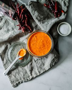 a glass jar filled with red chili sauce next to two spoons on a gray napkin