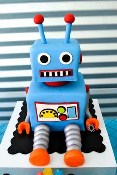 a blue robot cake sitting on top of a white plate with orange and black decorations