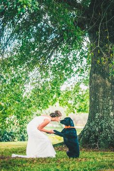 a bride and her dog are kissing under the shade of a large tree on their wedding day