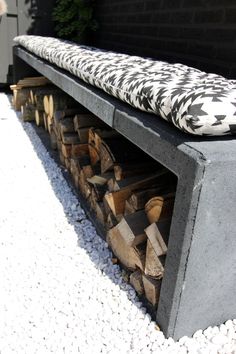 a bench made out of concrete with logs stacked on it's sides and an upholstered seat cushion