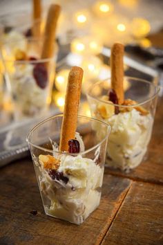 two cups filled with ice cream and cinnamon sticks on top of a wooden table in front of other desserts