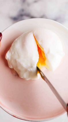 a person holding a spoon with some kind of food in it on a pink plate