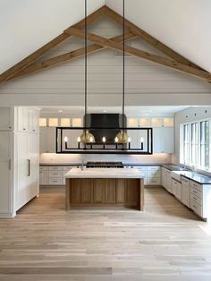 an open kitchen with wooden floors and white cabinets, wood beams on the ceiling, and two pendant lights hanging over the island