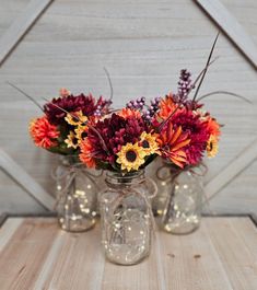 three glass vases with flowers in them sitting on a wooden table next to a barn door