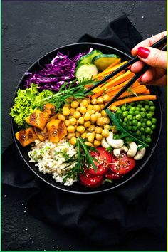 a person is holding chopsticks over a plate of vegetables and chickpeas