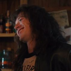 a man with long hair wearing a black leather jacket and smiling at someone in the background