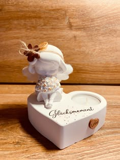 a small white figurine sitting on top of a heart shaped box with a candle in it