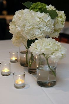 white flowers in vases and candles on a table