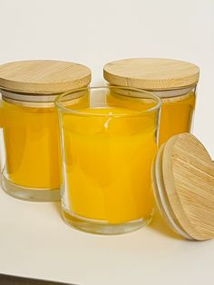 three jars filled with yellow liquid sitting on top of a white counter next to a wooden lid