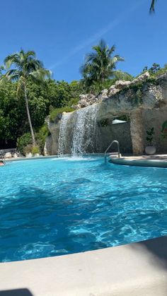 an outdoor swimming pool with waterfall in the middle and palm trees surrounding it on a sunny day