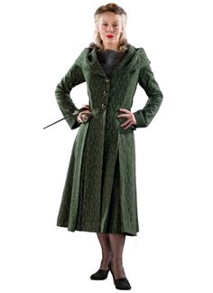 a woman in a green coat and black dress holding a wand with her hands on her hips