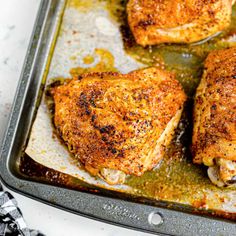 four pieces of chicken sitting on top of a baking pan covered in oil and seasoning