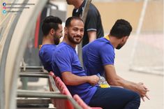 three men are sitting on the bleachers and one is holding a water bottle