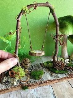 a miniature garden with moss and mushrooms in the shape of an old swing set, on a wooden table