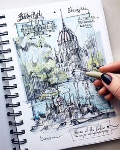 a hand is holding a pen and drawing on a page in a notebook with an image of a building