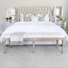 a large white bed sitting in a bedroom next to a dresser and mirror on the wall