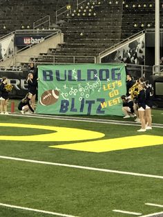 the cheerleaders are holding up a banner on the sidelines in front of an empty bleachers