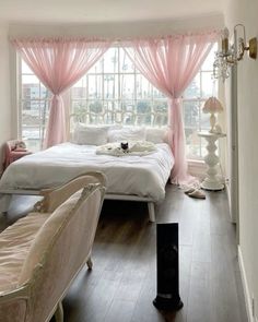 a cat is sitting on the edge of a bed in a room with pink curtains