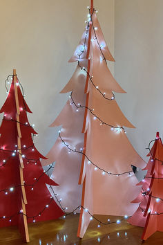 three christmas trees with lights on them in a room next to a wall and floor