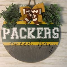 a wooden sign that says packers green bay with footballs on it and evergreen leaves