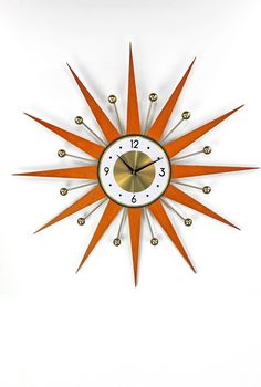 an orange and white clock with gold accents on the face is against a white background