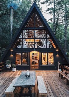 a - frame cabin in the woods with wood decking and large windows, surrounded by trees