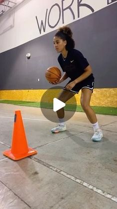 a woman holding a basketball standing next to an orange cone