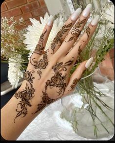 a woman's hand with henna tattoos on it and flowers in the background