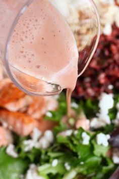 a person pouring dressing into a bowl full of salad greens and other ingredients to make the dressing