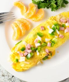 an omelet with ham, onions and cheese on a white plate next to orange slices