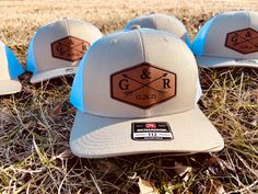 four hats sitting in the grass on top of some dry grass and one has a sticker that says g & r