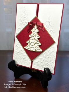 a red and white christmas card with a gold tree on the front, sitting on a black stand