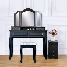 a black vanity with mirror, stool and vase on wooden floor next to white wall