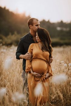 a pregnant couple cuddle in a field at sunset