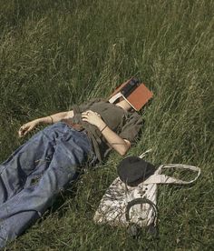 a person laying in the grass with a book and hat on his head next to a pair of scissors