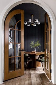 an arched doorway leads to a dining room with wood floors and black walls, along with a wooden table set for four