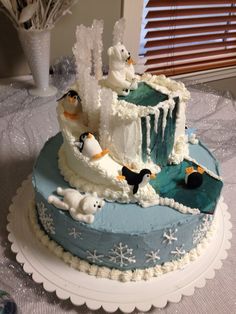 a cake with frosting and penguins on it sitting on a table next to a window