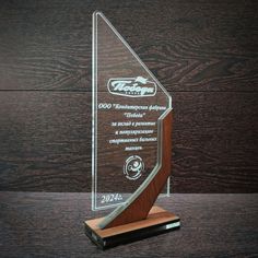 a glass trophy with a wooden base on a wood table next to a black wall