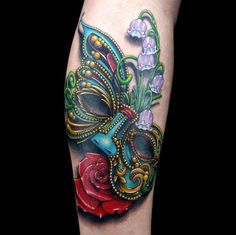 a close up of a tattoo with a mask and flowers on the leg, in color