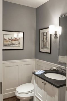 a white toilet sitting next to a sink in a bathroom under two framed pictures on the wall