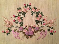 an embroidered wall hanging with pink flowers and green leaves in the center on a beige background