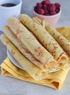 a stack of crepes sitting on top of a plate next to a bowl of berries