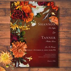 an orange and red floral wedding card on a wooden table with autumn flowers in the background