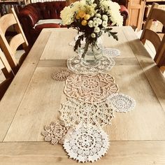 a wooden table topped with a vase filled with flowers and lace doily on top of it