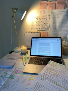 an open laptop computer sitting on top of a desk next to papers and a lamp