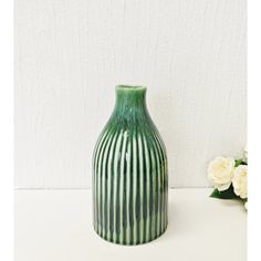 a green vase sitting on top of a table next to a white flower pot and wall