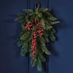 a christmas wreath hanging on the front door with berries and pine cones attached to it